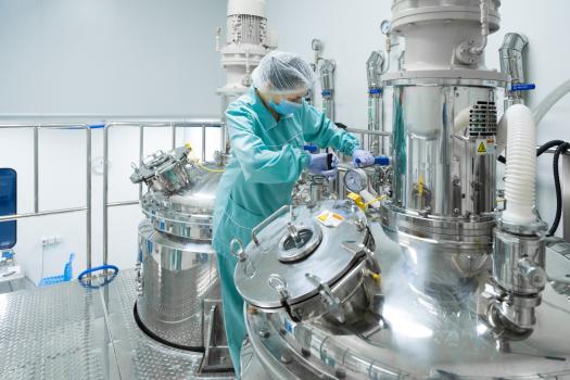 Pharmaceutical factory woman worker in protective clothing operating production line in sterile environment